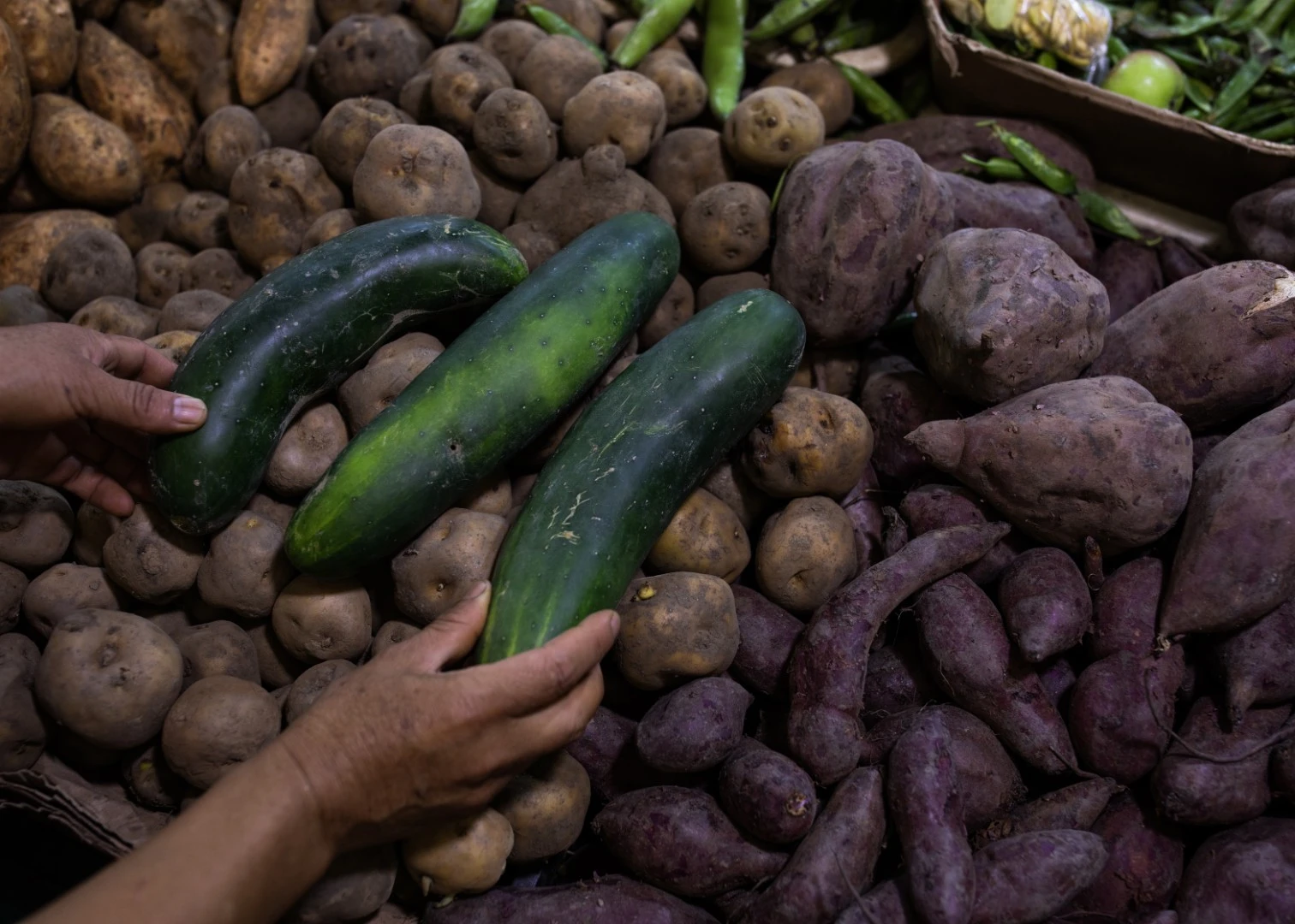 Puesto de mercado con papas, comotes y pepinos.