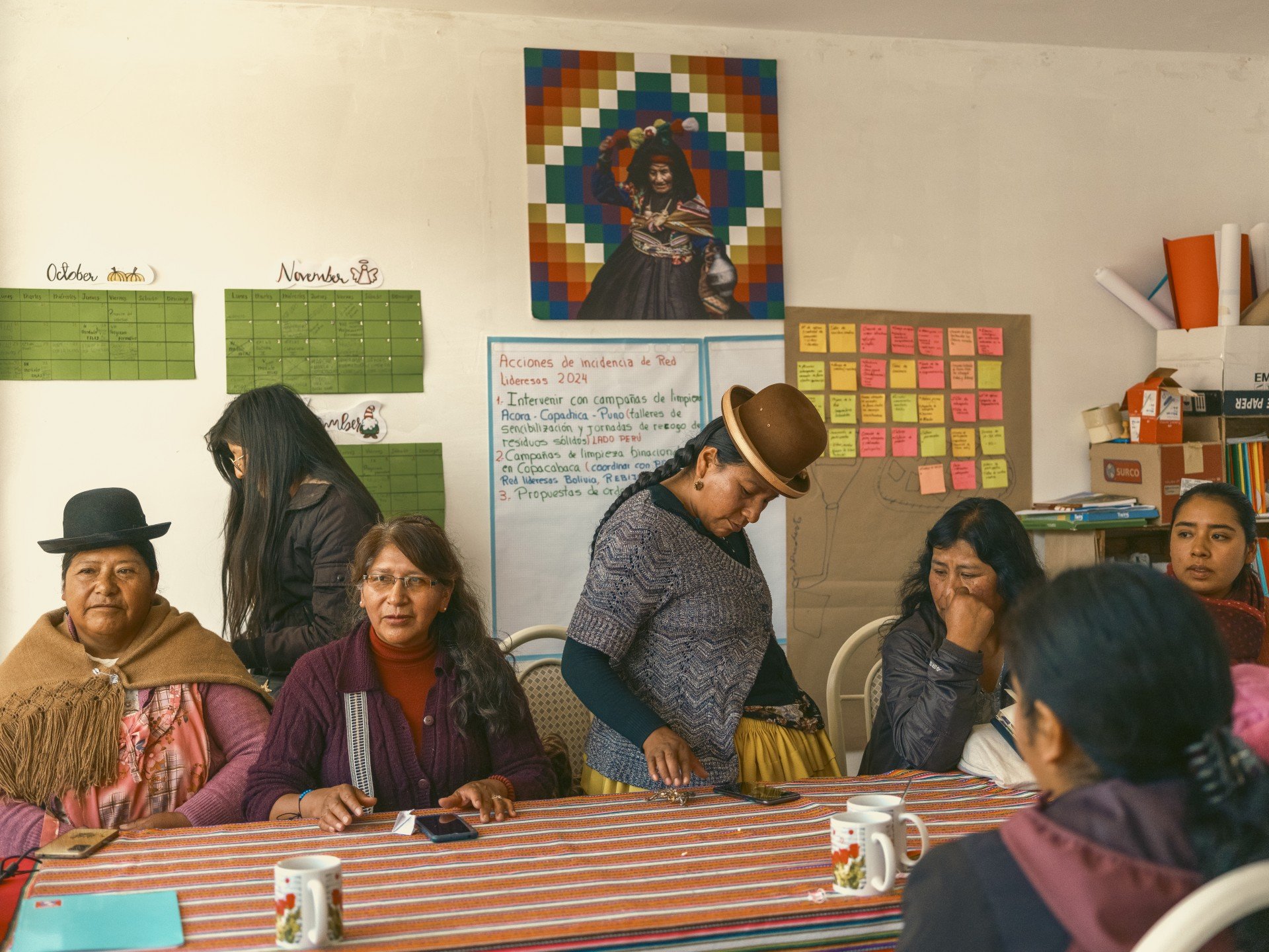 Fotoperiodismo documental mostrando a un grupo de mujeres y pobladores reunidos alrededor de una mesa roja en un espacio interior, debatiendo o revisando documentos.