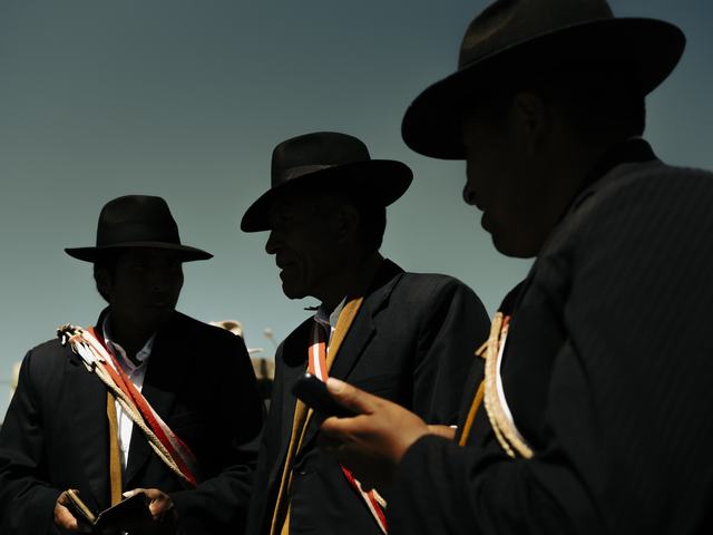 Siluetas oscuras de tres hombres (posiblemente autoridades o lancheros) con sombreros, conversando y mirando un teléfono contra un cielo dramático.