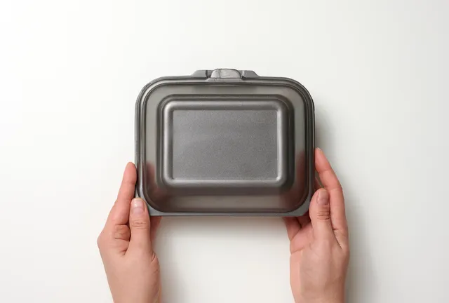 female-hand-holds-disposable-food-container-gray-box-of-polystyrene-on-white-background