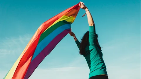 unrecognizable_young_girl_raising_gay_pride_flag_above_her_head.jpg