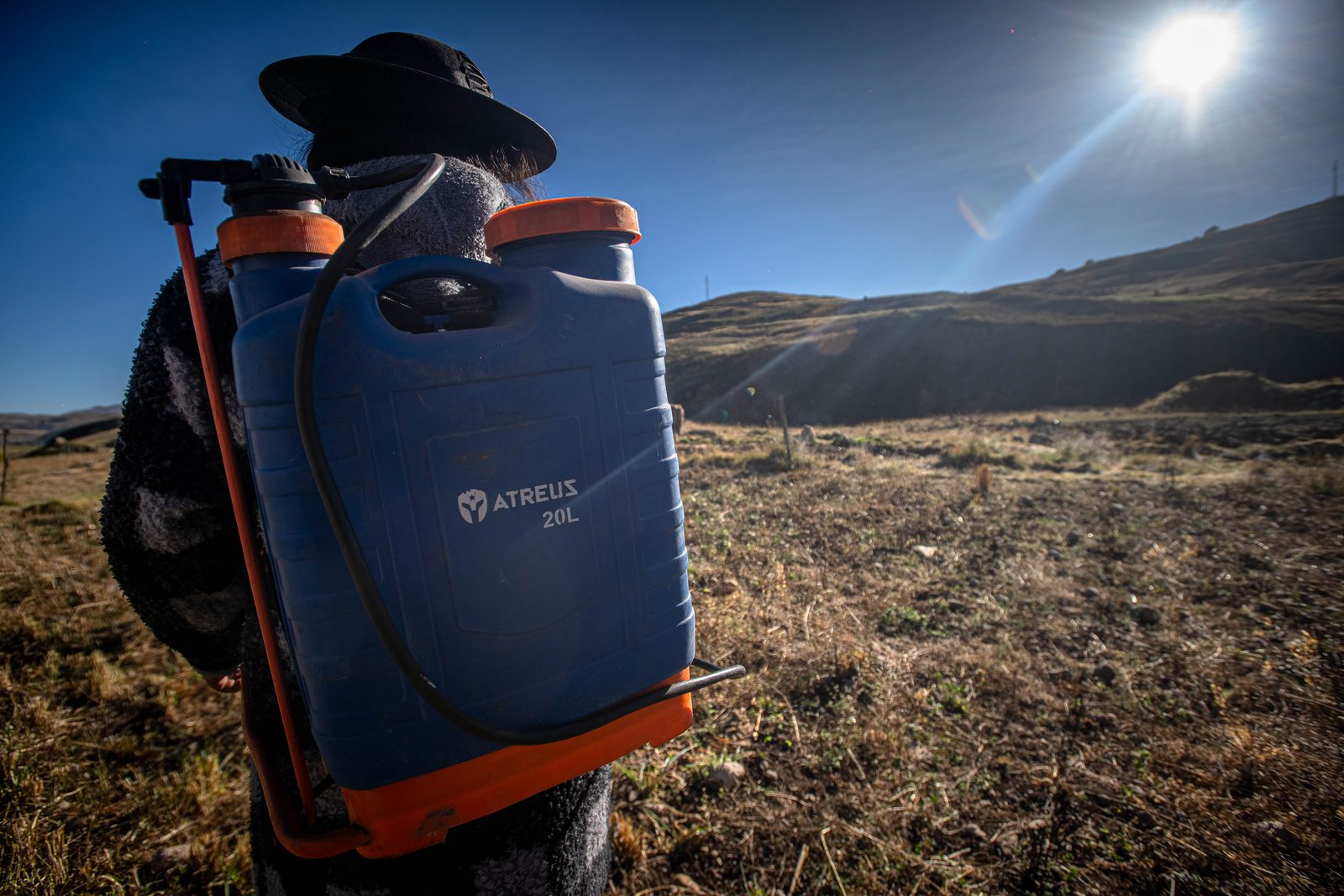 Una agricultora con la mochila fumigadora a la espalda, a contraluz